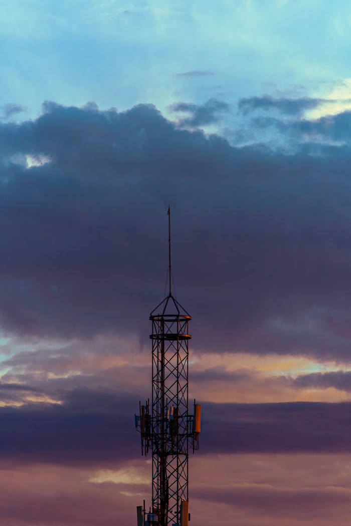 A lone radio mast silhouette against a dramatic, dusk sky with layered rain clouds.