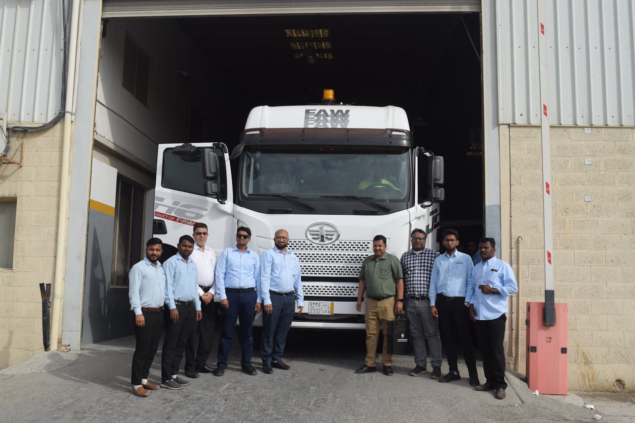 A group of people standing in front of a FAW truck parked at a warehouse entrance, showcasing teamwork.